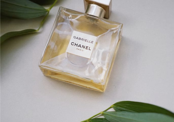 Chanel Gabrielle Essence perfume laying flat on a table with green leaves above and below it